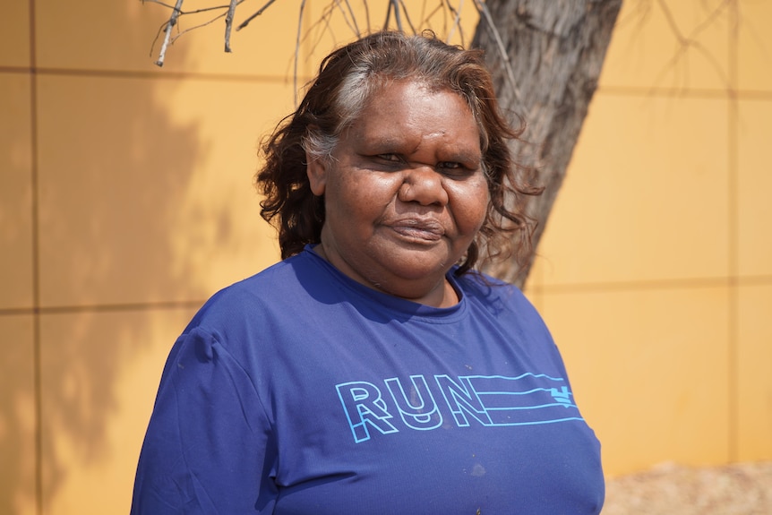 An Aboriginal woman stands in front of an orange wall