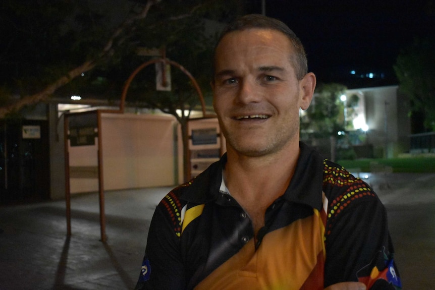 Nathan Coelli smiles at the camera. His hair is short and it is night time in Alice Springs.
