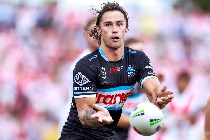A Cronulla Sharks NRL player passes the ball to his right against St George Illawarra Drgaons.