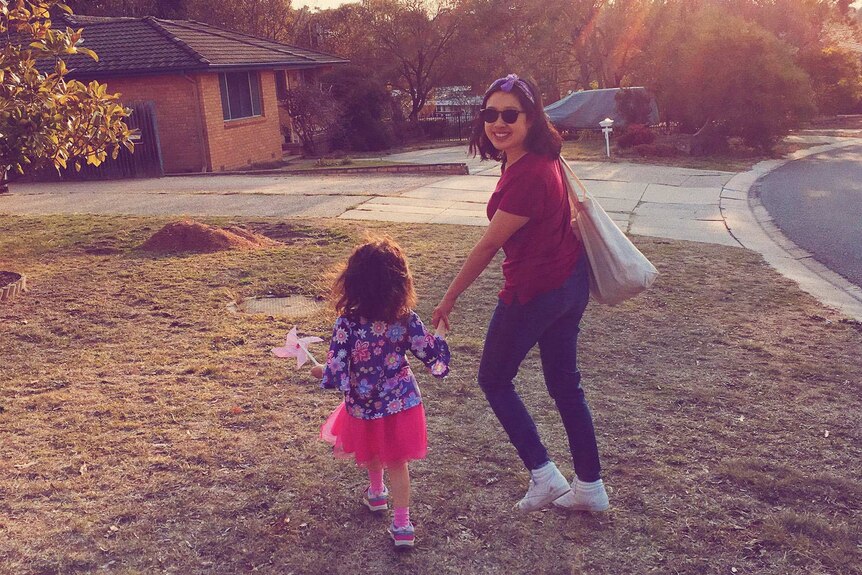 Carla Gee holding hands with her daughter, who has her back to the camera, outside a suburban brick house