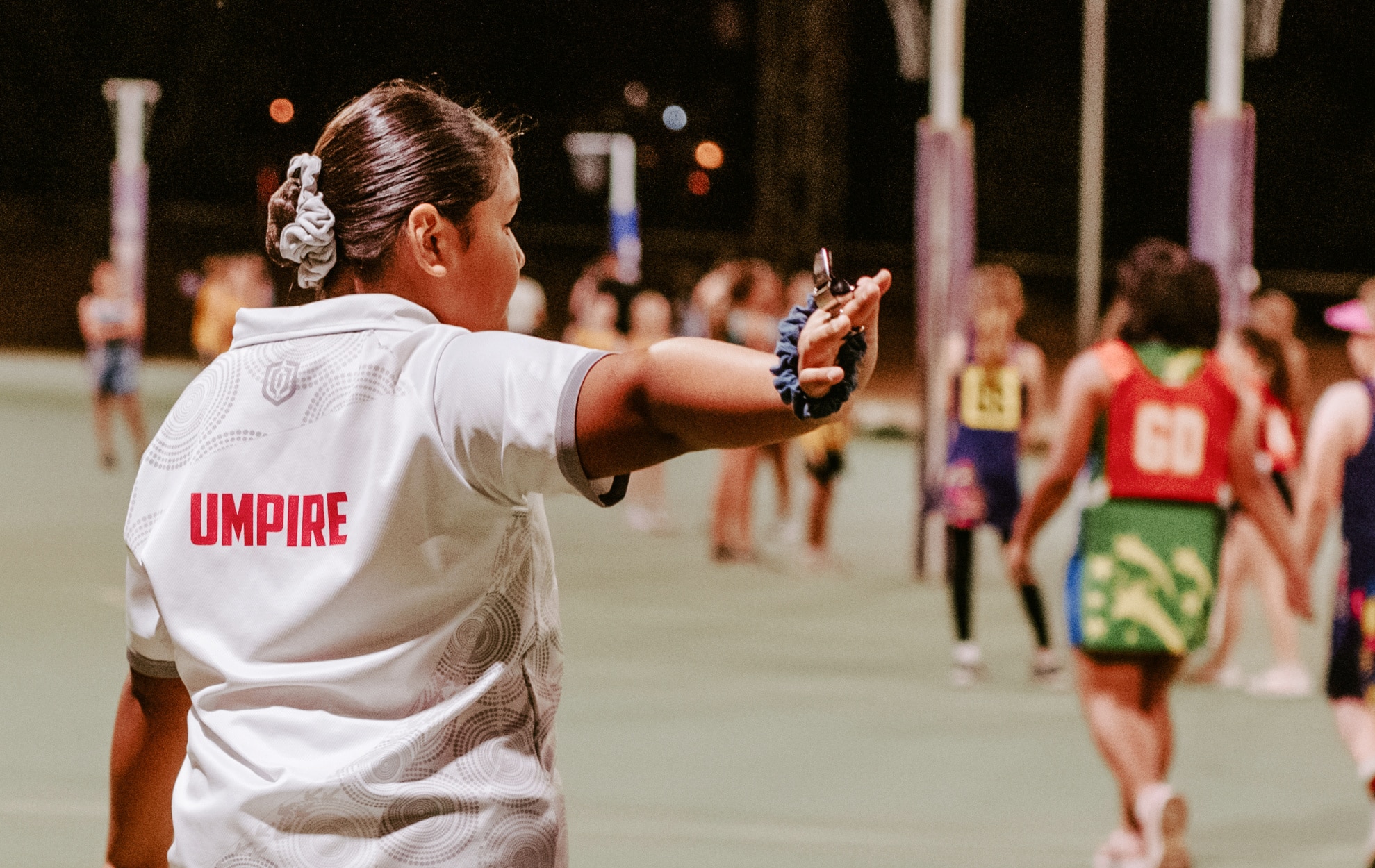 A young girl with dark hair umpires a netball game in white clothing