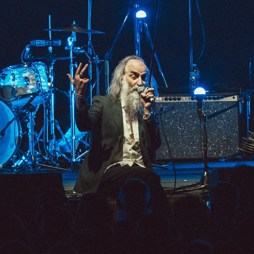 Dirty Three's Warren Ellis sits at front of Hamer Hall stage, speaking to the audience, flanked by Jim White and Mick Turner.