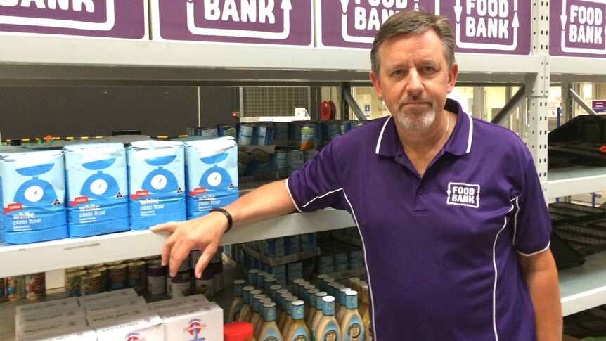Foodbank WA CEO Gary Hebble stands in a purple shirt in front of stocked shelves.