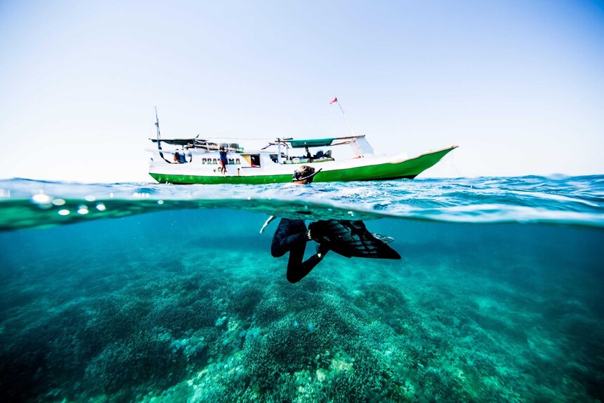 A woman with a snorkel swims near a boat, we can see her fins underwater
