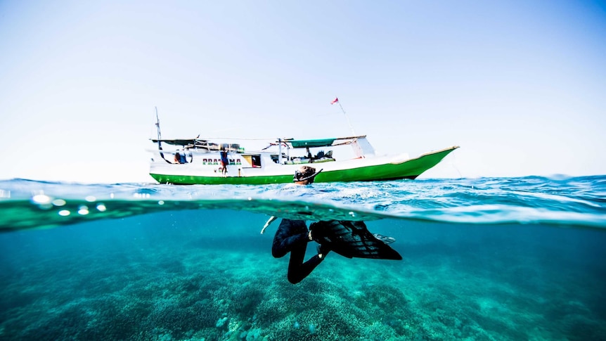 A woman with a snorkel swims near a boat, we can see her fins underwater