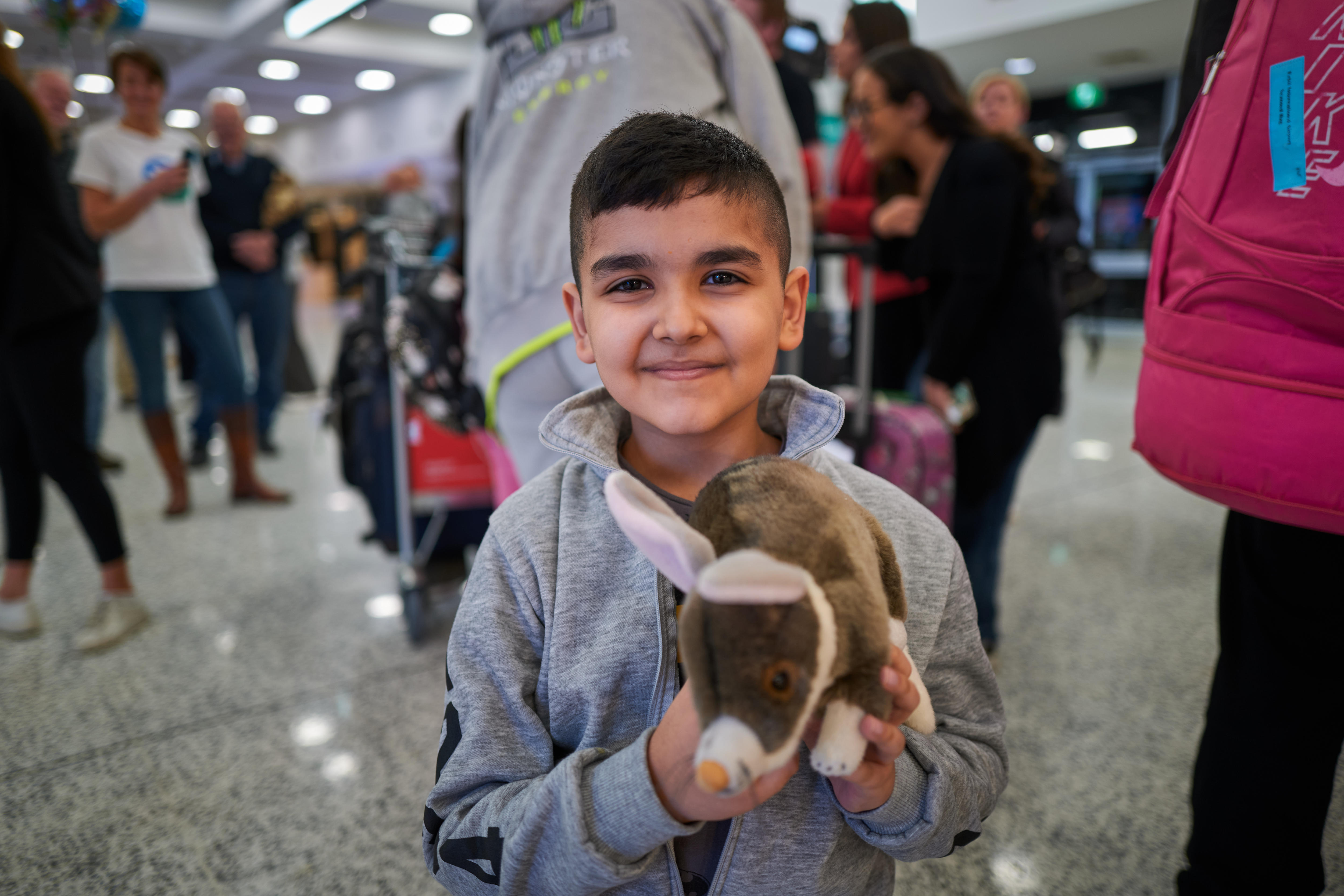 一个小男孩在机场到达区微笑着拿着一个毛绒玩具
