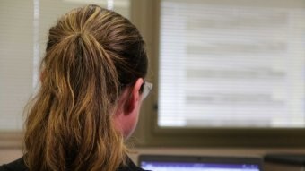 A woman with her hair in a ponytail looks at a laptop