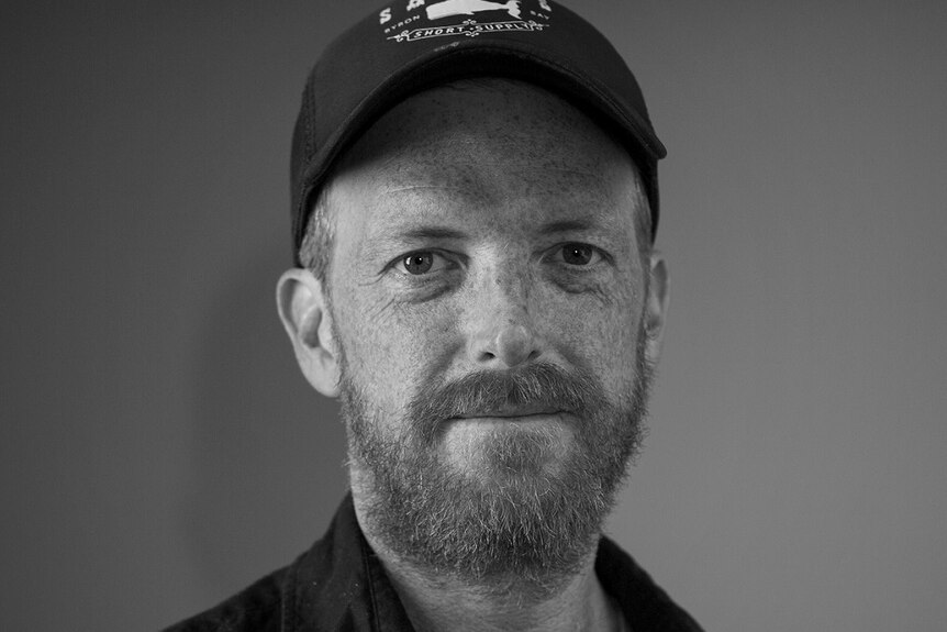 A black and white portrait photo of a man with a beard in a cap.