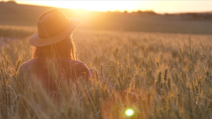 Woman with hat standing in her crop in the bright warm morning sun