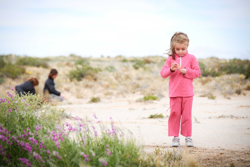 Little girls pick flowers in the desert.