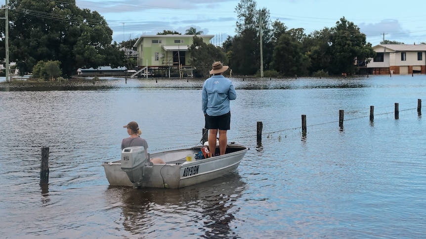 a man standing up in a dinghy with a woman sitting in it as he paddles down a flooded street