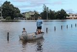 a man standing up in a dinghy with a woman sitting in it as he paddles down a flooded street