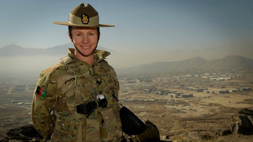 A woman in military uniform in front of desert landscape. 