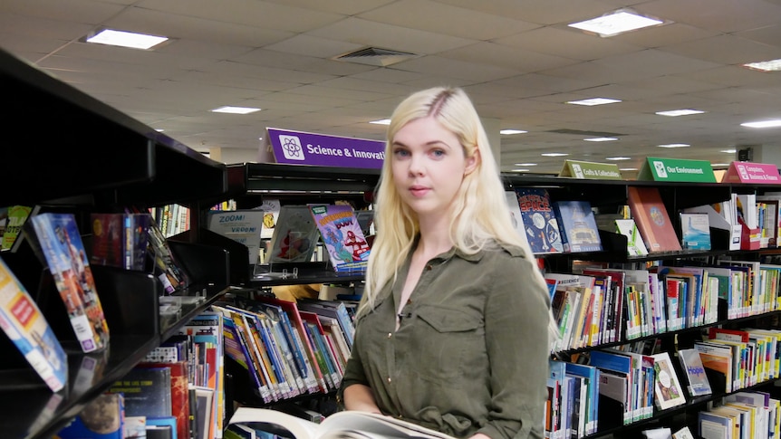 Tutor Angela Fleming holds a book and stands in front of a library shelf.