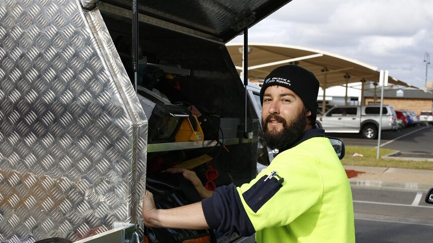 An electrician stands at the side of his ute and is about to get his tools