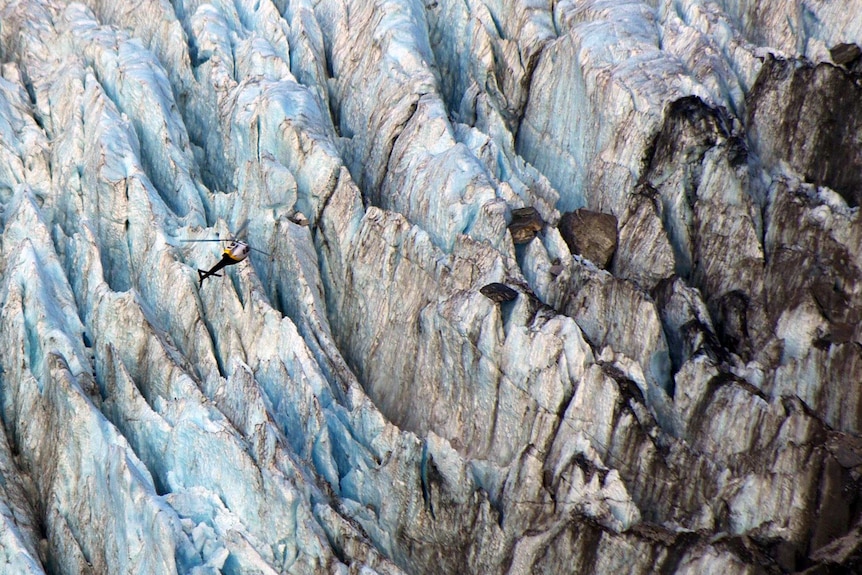 A helicopter hovers over the rugged terrain of the Franz Josef Glacier.