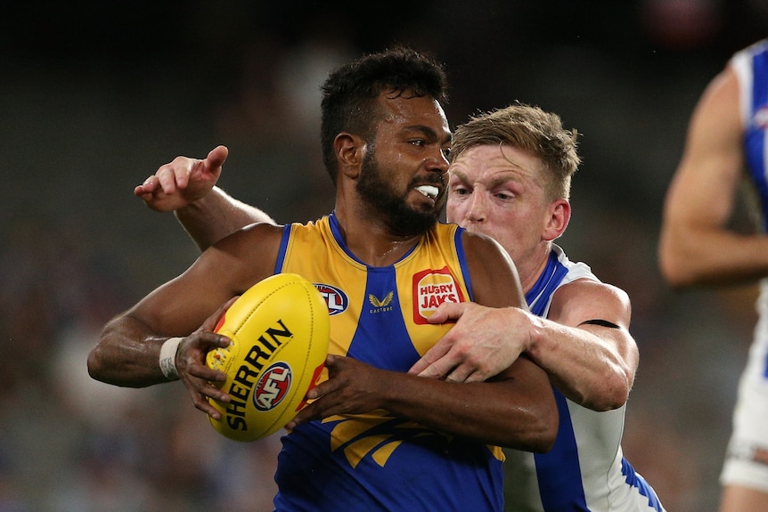 An AFL player carrying the ball tries to shrug off a tackler.