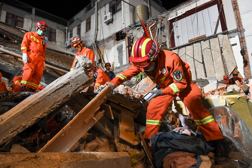Rescuers dressed in orange suits climb the rubble of the collapsed hotel looking for survivors. 