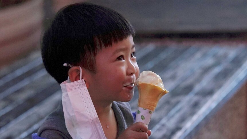 A child with a face mask eats an ice cream outside an ice-cream store