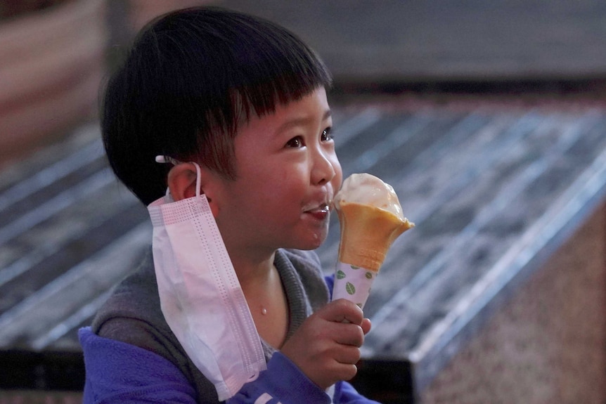 A child with a face mask eats an ice cream outside an ice-cream store