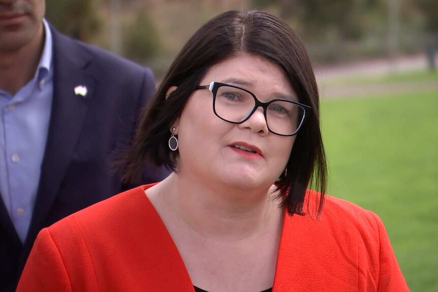 A woman wearing black glasses and a red top looks sternly down the camera.