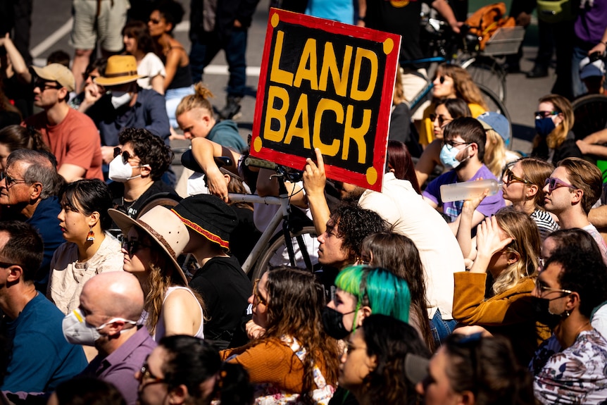A protester holds up a sign saying 'LAND BACK' at a sit-in at Flinders Street Station.