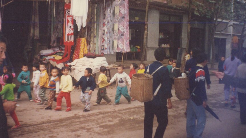 Children hold hands as they walk down a street in China in the 1980s.