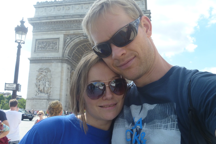 Una pareja está sonriendo y de pie frente al gran monumento del Arco de Triunfo en París.