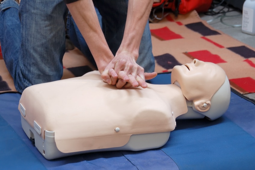 A person performs chest compressions on a CPR dummy.