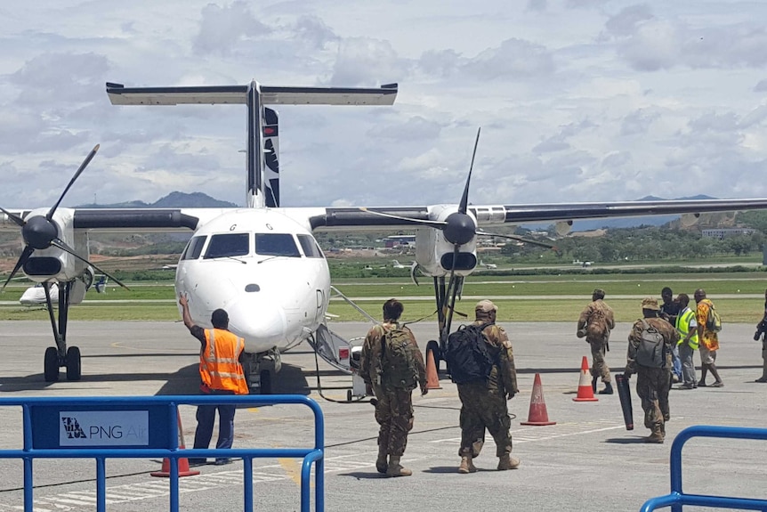 A plane sits on a tarmac before police and soldiers board