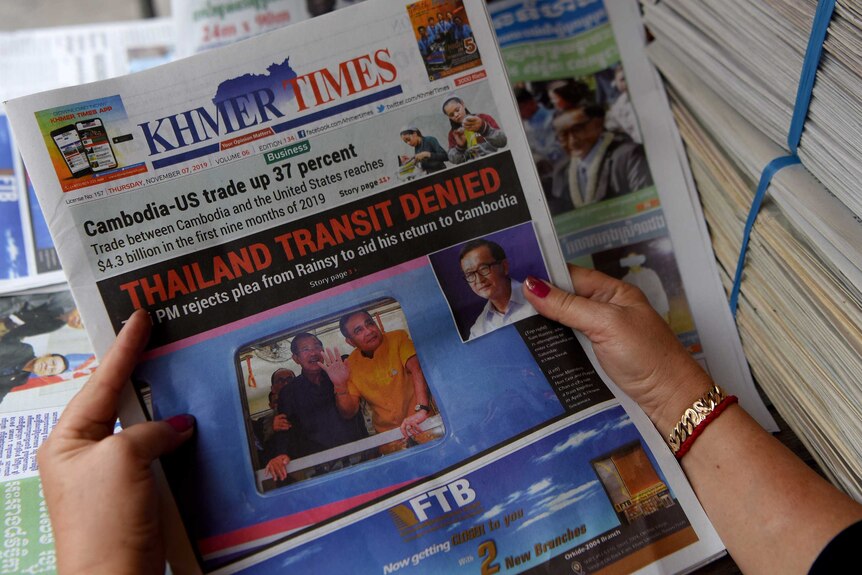 A woman's hands holds the Khmer Times English newspaper in Cambodia, with a headline reading 'Thailand Transit Denied'.