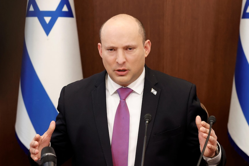 Man in a suit with an Israel flag in the background speaks
