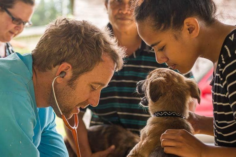 Geoff Neal, the lead veterinarian for SPAW, does a check up on a little brown dog being held by a woman.