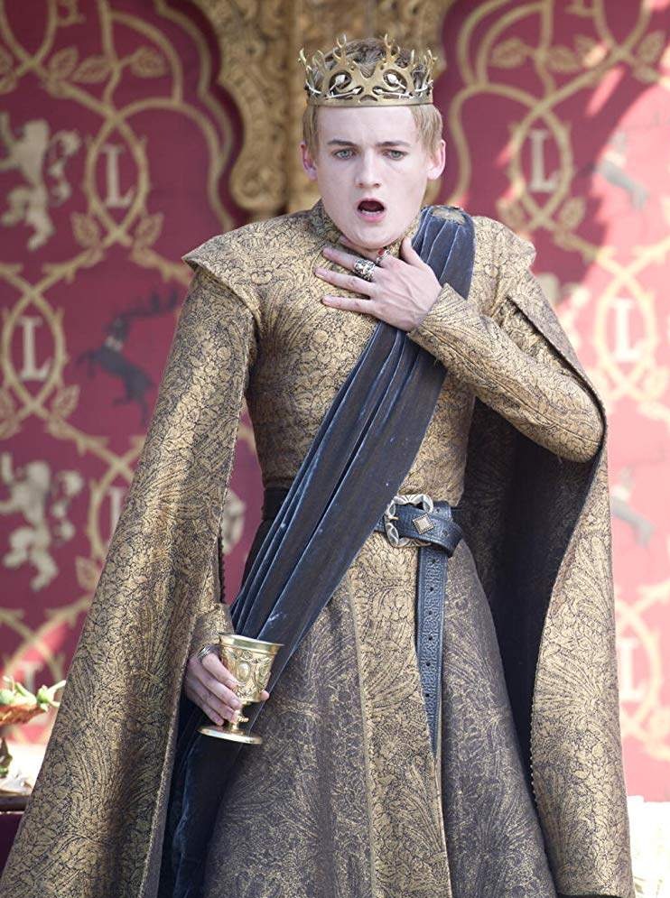 Joffrey Lannister clutches his throat as he wears golden robes and holds a poisoned goblet in his other hand.