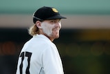 A man with long hair and a cricket cap smiles during a game. 