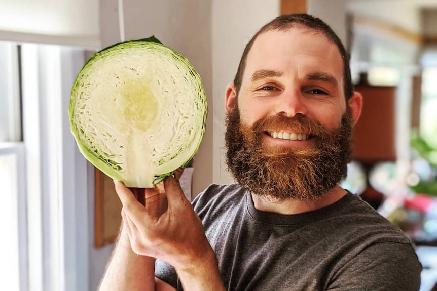 Hobart man Dusty Moore holds half a homegrown cabbage close to his face, his smiling at the success of his veggie patch.