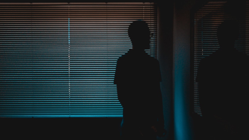 Man standing near a wall in darkness.