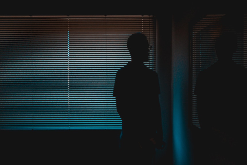Man standing near a wall in darkness.