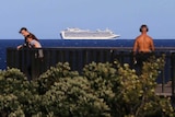 A cruise ship watched by two people on the shore