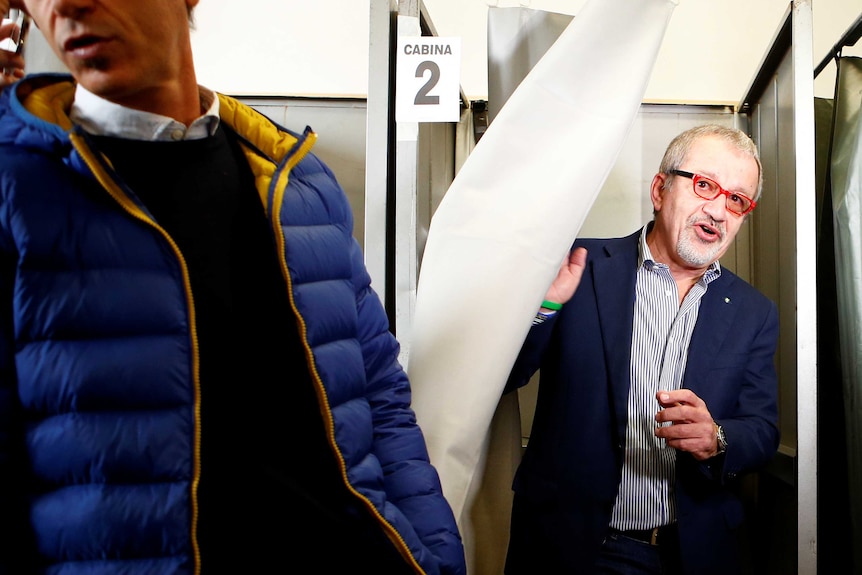 A man pulls across a curtain as he looks out from a voting booth