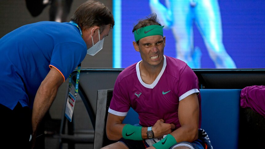 Rafael Nadal holds his abdomen and grimaces as he talks to medical staff on court