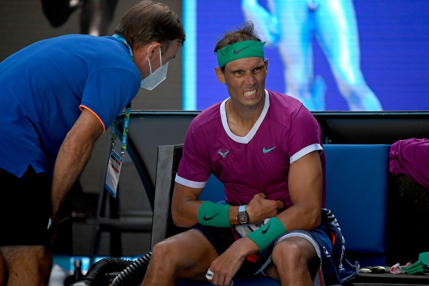 Rafael Nadal holds his abdomen and grimaces as he talks to medical staff on court