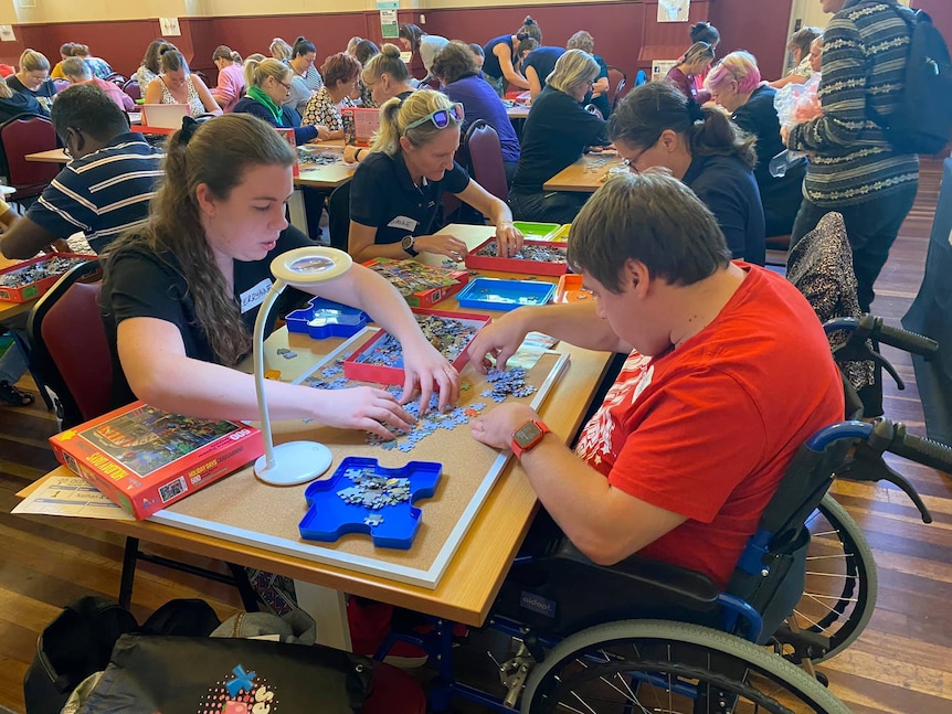 A man in a wheelchair and a woman sit at a table and compete as a pair in a jigsaw competition