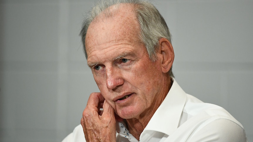 Wayne Bennett scratches his chin with a neutral expression on his face