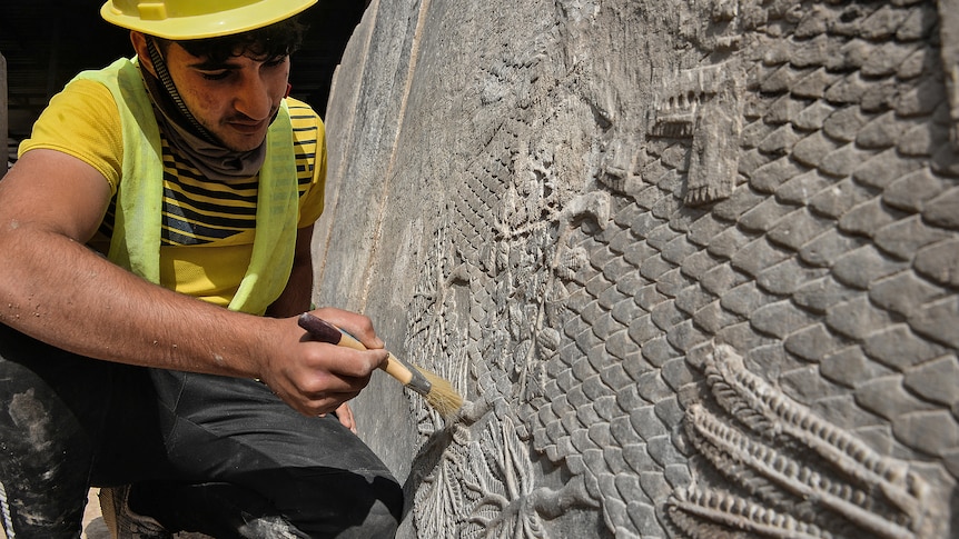 A man holds a brush up to the rock carving. 