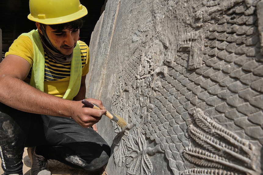 A man holds a brush up to the rock carving. 