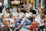 A group of people, including breastfeeding mothers, sitting and standing in a shopping centre