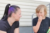 A mum with her hair in a pony tail talks to her young son who has blonde hair