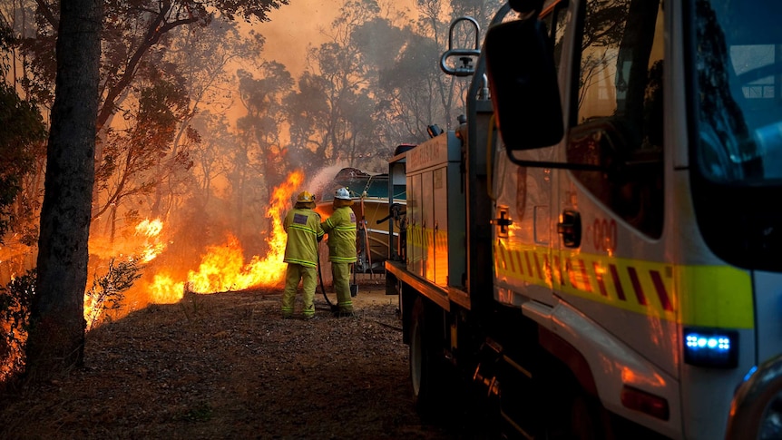 Bushfire brigade volunteers protecting a boat at the rear of a house, with a truck in the foreground.