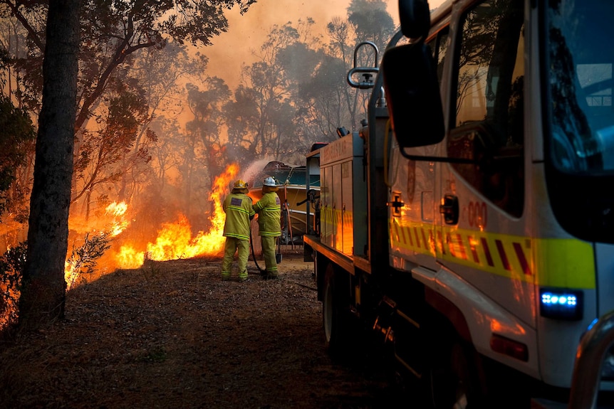 Bushfire brigade volunteers protecting a boat at the rear of a house, with a truck in the foreground.